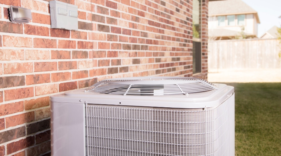 Air conditioning unit installed outside a brick wall, emphasizing HVAC maintenance and cooling solutions for residential properties.