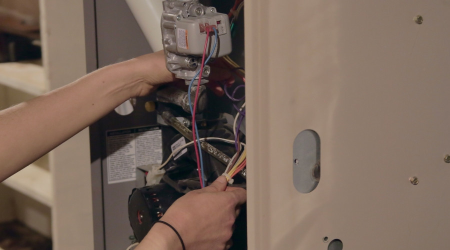 Technician performing maintenance on a furnace, adjusting wires and components for HVAC service.